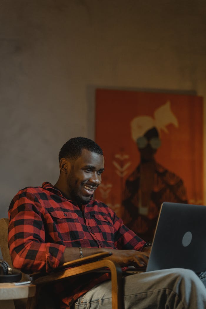 African American man in plaid shirt working on a laptop at home, creating a cozy atmosphere.