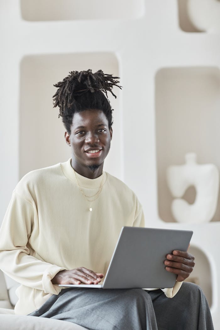 Smiling man with afro hair working on a laptop in a modern indoor setting.
